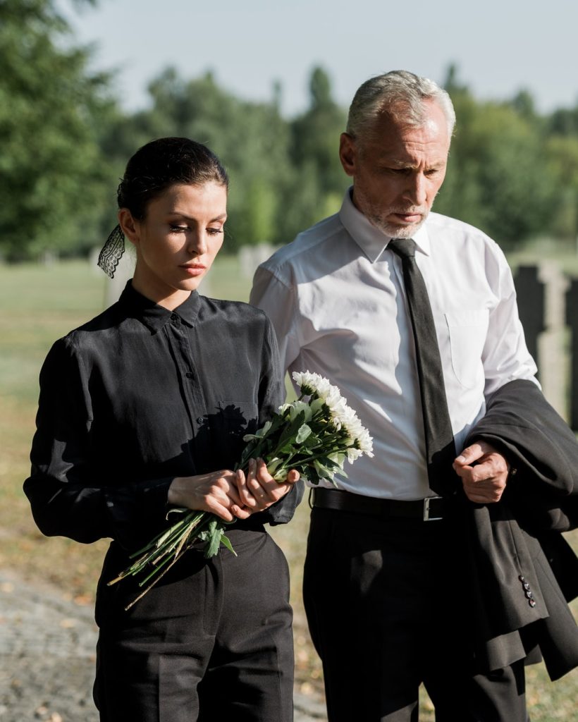 homme âgé barbu marchant près d'une femme tenant des fleurs lors d'un enterrement