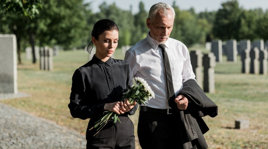 homme âgé barbu marchant près d'une femme tenant des fleurs lors d'un enterrement